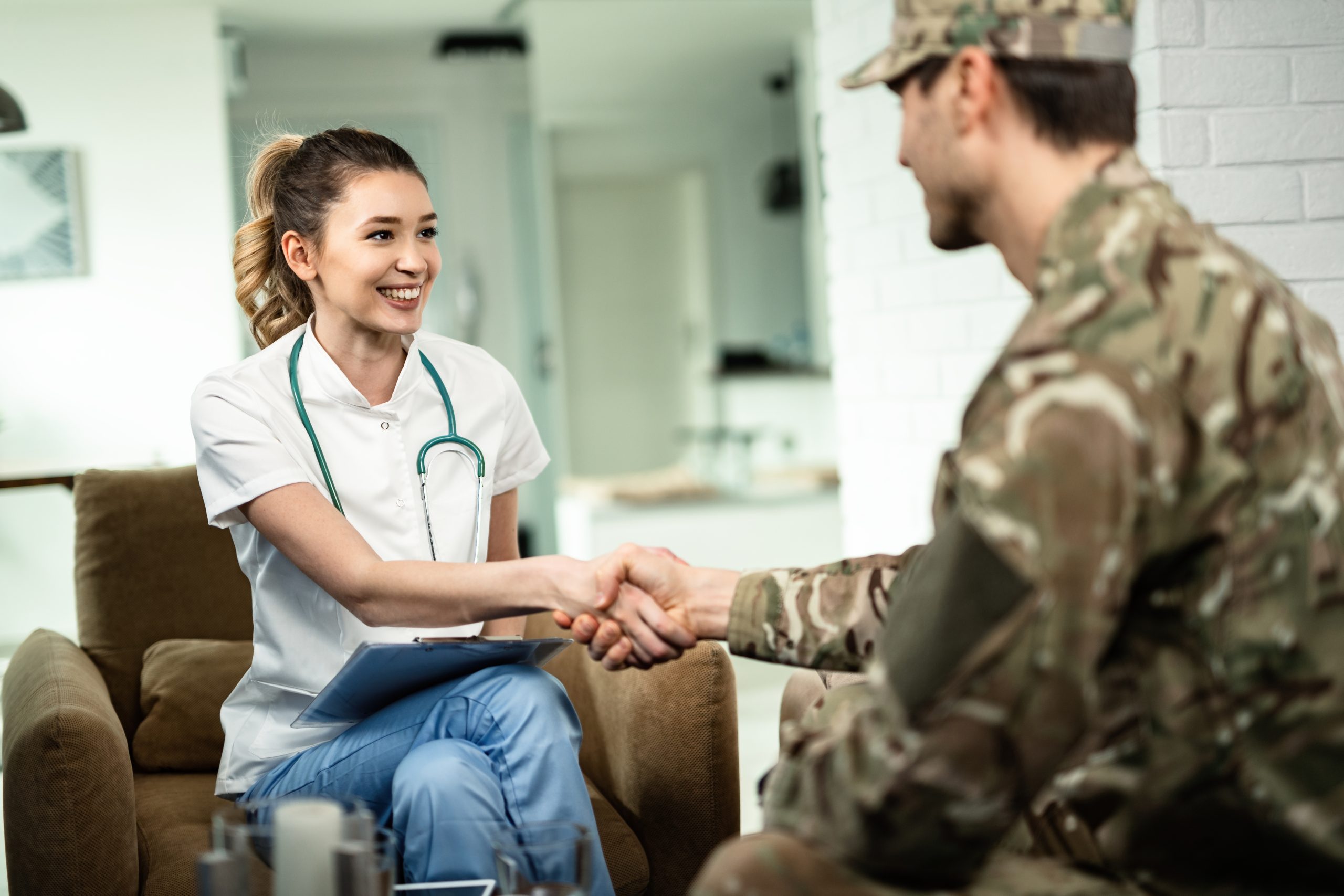 Happy female doctor and military man shaking hands while meeting at his home.