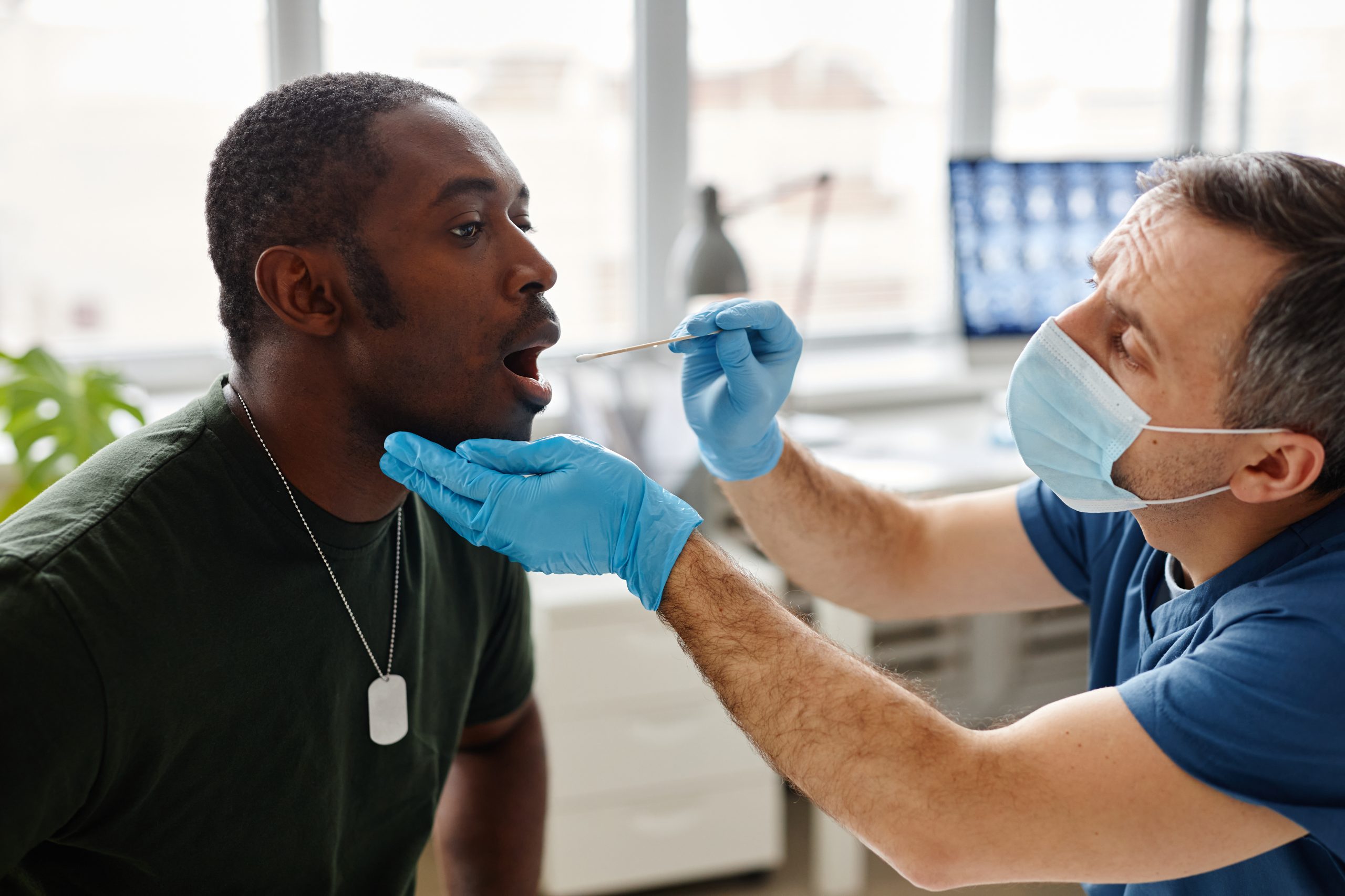 Young Black military officer sitting with mouth wide open doing PCR swab test for coronavirus in modern hospital